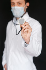 Male Doctor on a black background with a stethoscope in his hands close-up