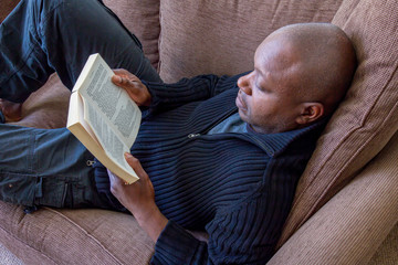Black man, of African ethnicity, reading on the sofa