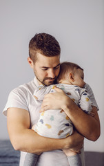 Portrait of attractive unshaven young father holding his only beloved son and putting him to sleep....