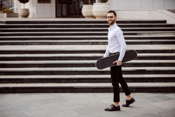 Fototapeta na wymiar Full length of man in shirt walking outdoors and holding skateboard under armpit.