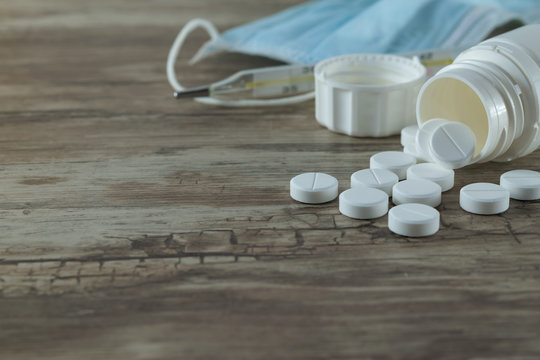 Tablets in a white jar, a thermometer, a medical mask to protect against flu and  viral diseases. Protective mask on a wooden background against the spread of coronavirus and epidemic. Coronavirus