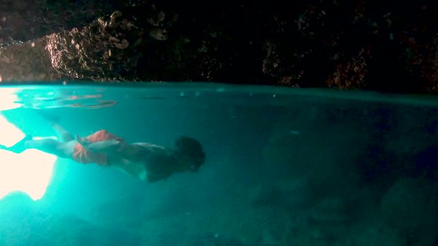 A young athlete man swims underwater into the cave with nice lighting