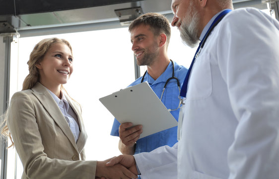 Two doctors and female patient shaking hands before consultation in the office of a modern medical center.