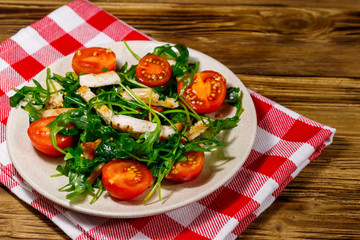 Tasty salad of fried chicken breast, fresh arugula and cherry tomatoes on wooden table