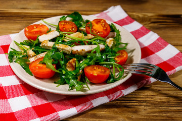 Tasty salad of fried chicken breast, fresh arugula and cherry tomatoes on wooden table
