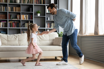 Full-length view loving gentleman father invites on dance little princess daughter, kid girl wearing pink fluffy skirt and crown holds dad hand enjoy time together having fun on active weekend concept © fizkes