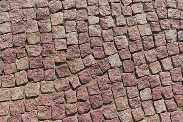 The surface of the path is paved with square-shaped granite cobblestones. The stones are laid in several rows on the sand. All tiles are uneven and of different shapes. Background, texture, backdrop.