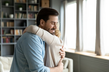 Caring attentive grown up son visited mother, older mom hugs adult millennial child she missed him enjoy moment, relatives people standing inside of cozy living room feels happy, family bonds concept