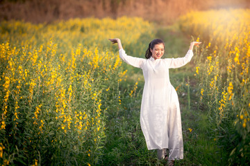 Naklejka na ściany i meble Asian women in Vietnamese clothes jump with joy in the Juncea Crotalaria flower fields.