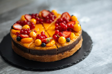 Closeup on organic tangerine cake decorated with berries on the light grey background, horizontal