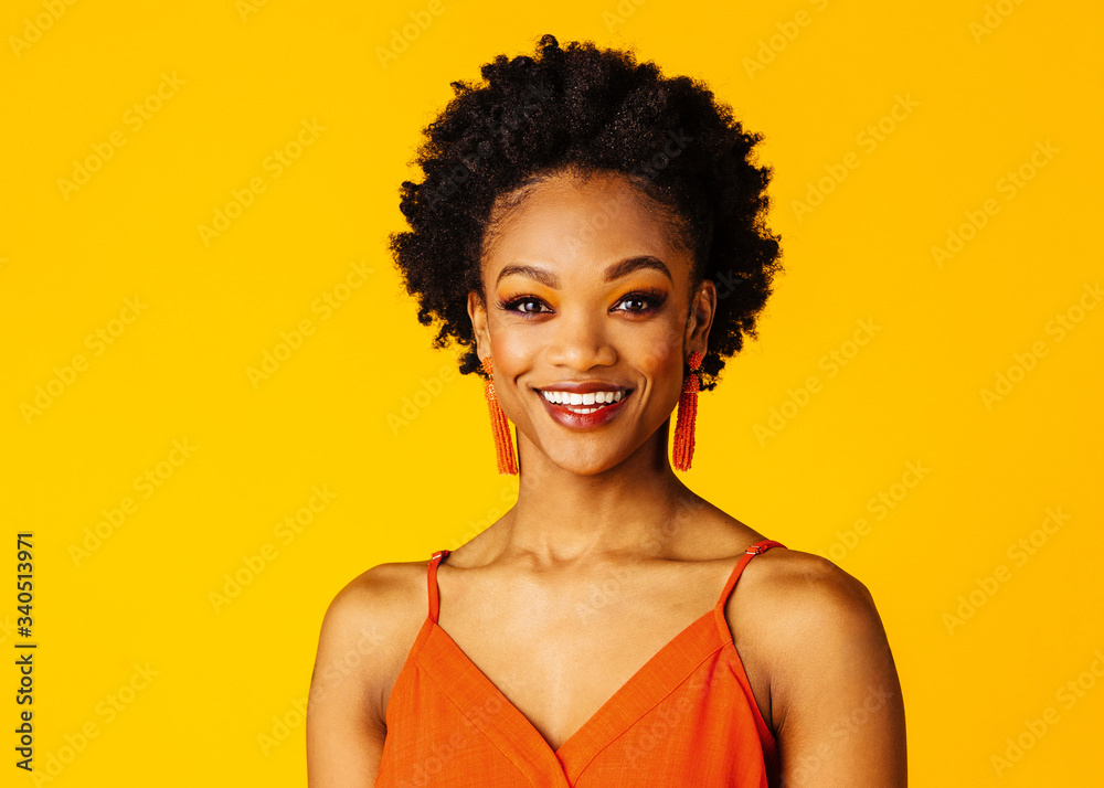 Wall mural portrait of a smiling young woman with orange tassel beaded earrings on yellow color background - Wall murals