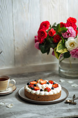 Side view on appetizing sweet cake with white cream and decorated with berries on the grey background with a cup of tea, vertical