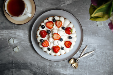 Top view on appetizing sweet cake with white cream and decorated with berries on the grey background, horizontal