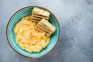 Turquoise bowl with polenta and fried cheese, top view on a light-blue stone background with space, horizontal shot