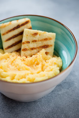 Close-up of polenta with roasted cheese served in a turquoise bowl, selective focus, vertical shot
