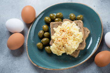 Turquoise plate with scrambled eggs cooked in british style with bread slices and green olives, horizontal shot