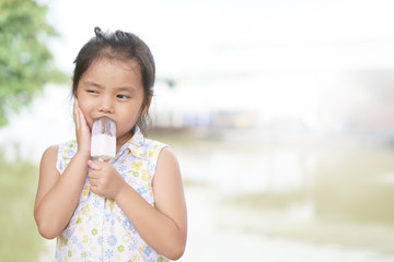 Asian child hypersensitive teeth or kid girl enjoy delicious eating and holding chocolate ice cream stick for sweet dessert and toothache with hand to cheek on summer holiday travel with white space