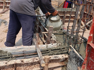 Close up of industrial worker pouring cement or concrete with plastic buckets at new construction site.