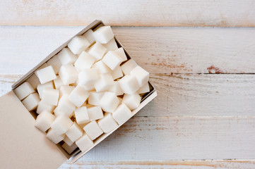 Refined sugar cubes in a cardboard box shot on a white painted wooden surface.