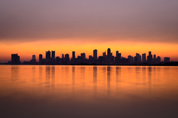 Fototapeta na wymiar Silhouette of high rise buildings in Seef district during sunrise with beautiful reflections, Manama, Bahrain
