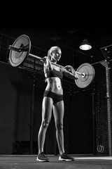 Full height black and white photo of fitness woman exercising with barbell in a gym. Muscular caucasian woman using curved barbell at fitness club. Shot of a strong woman in sportswear.