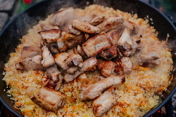 Rice with pork ribs in a cast iron skillet over a fire. Pilaf is cooked in a cast-iron pan. Pilaf is a traditional Middle Eastern and Asian food.