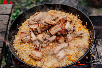 Rice with pork ribs in a cast iron skillet over a fire. Pilaf is cooked in a cast-iron pan. Pilaf...