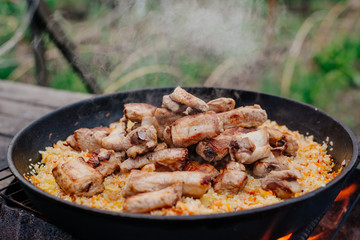 Rice with pork ribs in a cast iron skillet over a fire. Pilaf is cooked in a cast-iron pan. Pilaf is a traditional Middle Eastern and Asian food.