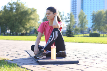 Beautiful young woman looking away while sitting on exercise mat at park, relaxing after training.