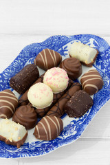 Selection of chocolates on a blue and white patterned plate.  On a white wood background