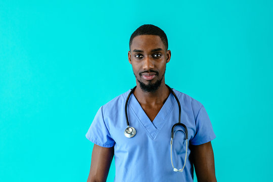 Portrait Of A Serious Male Doctor Or Nurse Wearing Blue Scrubs Uniform And Stethoscope, Isolated On Blue Background