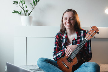 Girl sitting at home learns to play ukulele using online lessons.