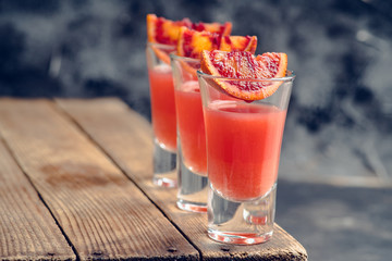 Strong red cocktail in shots on the rustic background. Selective focus. Shallow depth of field.