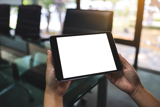 Mockup image of hands holding and using black tablet pc with blank white desktop screen in the office