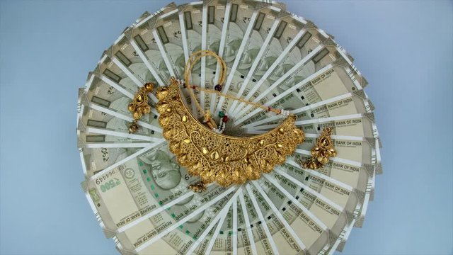 Top view shot of five hundred banknotes with jewels - gold loan or gold mortgage. Closeup shot of 500 Indian currency notes revolving on a turntable with gold jewelry against the blue platform