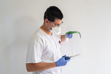 Naklejka premium Doctor / nurse cutting a face shield with scissors to protect against the coronavirus. He is a young man. He wears gloves, masks, and glasses. He wears a white uniform.