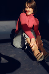 Beautiful girl in a studio. Stylish girl sitting on the floor. Lady in a red sweater.
