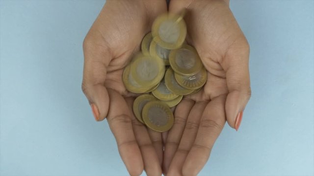 Closeup shot of Indian 10 rupee coins falling in the hands of a young woman. Top view shot - Two hands of a female held together while catching lots of ten Indian rupee coins against the blue backg...