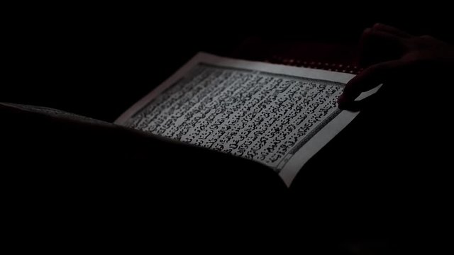 Muslim kid is learning to read The Quran in the dark room of rural house. Ramadan theme, or other Islamic spiritual events.