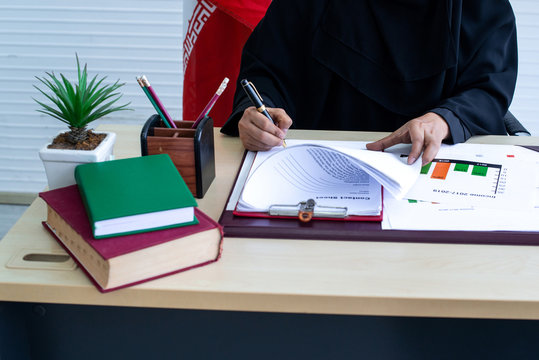 Arabian businesswoman in niqab or black garment (abaya) works in the office, signing document on the table