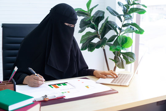 Arabian businesswoman in niqab or black garment (abaya) works in the office on the desk is a laptop