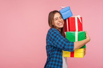 Portrait of excited happy girl in checkered shirt embracing lot of christmas gifts and smiling joyfully, celebrating birthday, admiring many presents. indoor studio shot isolated on pink background © khosrork