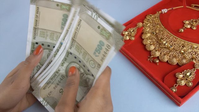 Young female counts a bundle of Indian currency notes - gold loan or gold mortgage. Closeup shot of woman hands counting 500 rupees banknotes with a jewelry box in the background - pawnshop concept