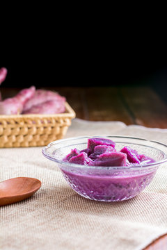 Purple sweet potato with coconut milk in transparent bowl on wooden table on black background. Delicious Thai dessert.