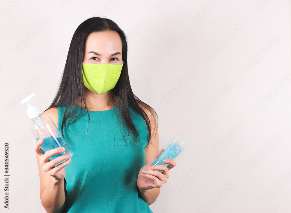 Wall mural asian woman wearing green polka dot fabric mask and green no sleeve t-shirt, holding two bottles of 