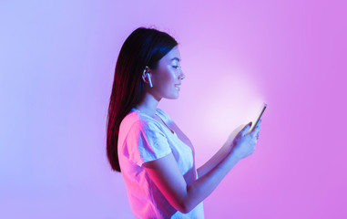 Woman with wireless headphones look at glowing smartphone © Prostock-studio