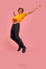 Full length vertical photo of stylish happy dark-skinned man celebrate his hands up broadly jumping on air, over pink background. Expressive hurrying up, sale, shopping. Emotions, ad concept