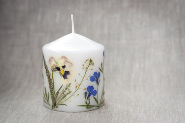 Candle with herbarium flowers on the linen cloth