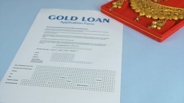 Closeup shot of a blank Gold loan application form - pawnshop concept in India. Pan shot of woman hands placing a bundle of Indian currency notes next to the form and a jewelry box on a blue backgr...