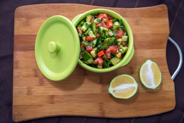 Chopped cucumber tomato salad in a green bowl. Lemon cut in half . fresh vegetable salad with tomato, cucumber and green onion on Cutting board.